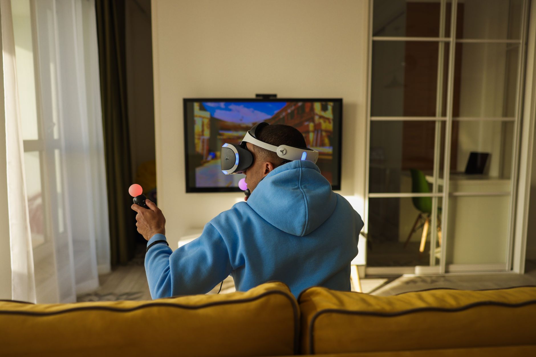 Person playing an immersive PC game with a controller, and someone else playing a mobile game, showing dual platform engagement.